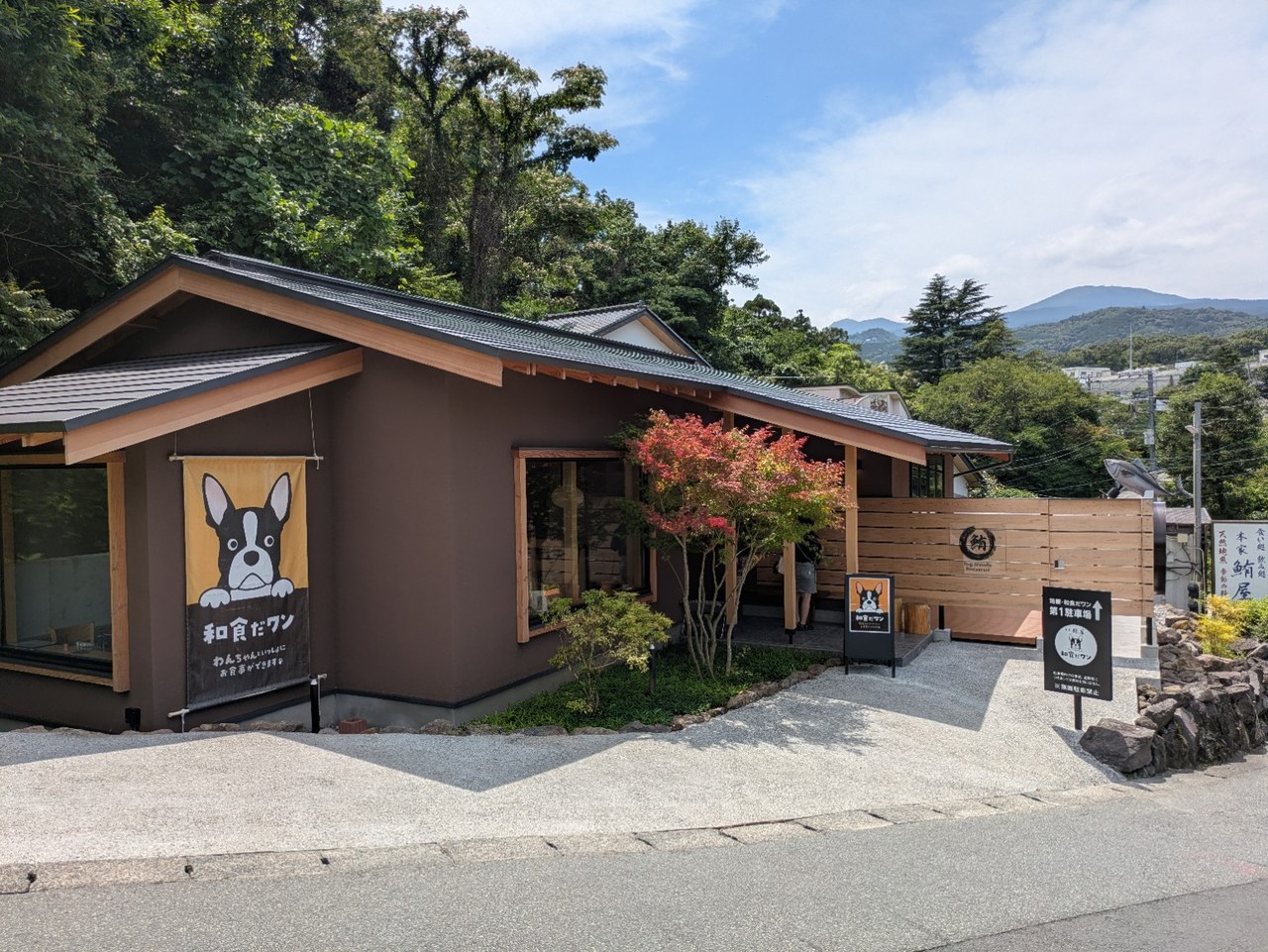 犬のイラスト入りの幕が掛かった和食だワンの建物と、奥に見える山並み