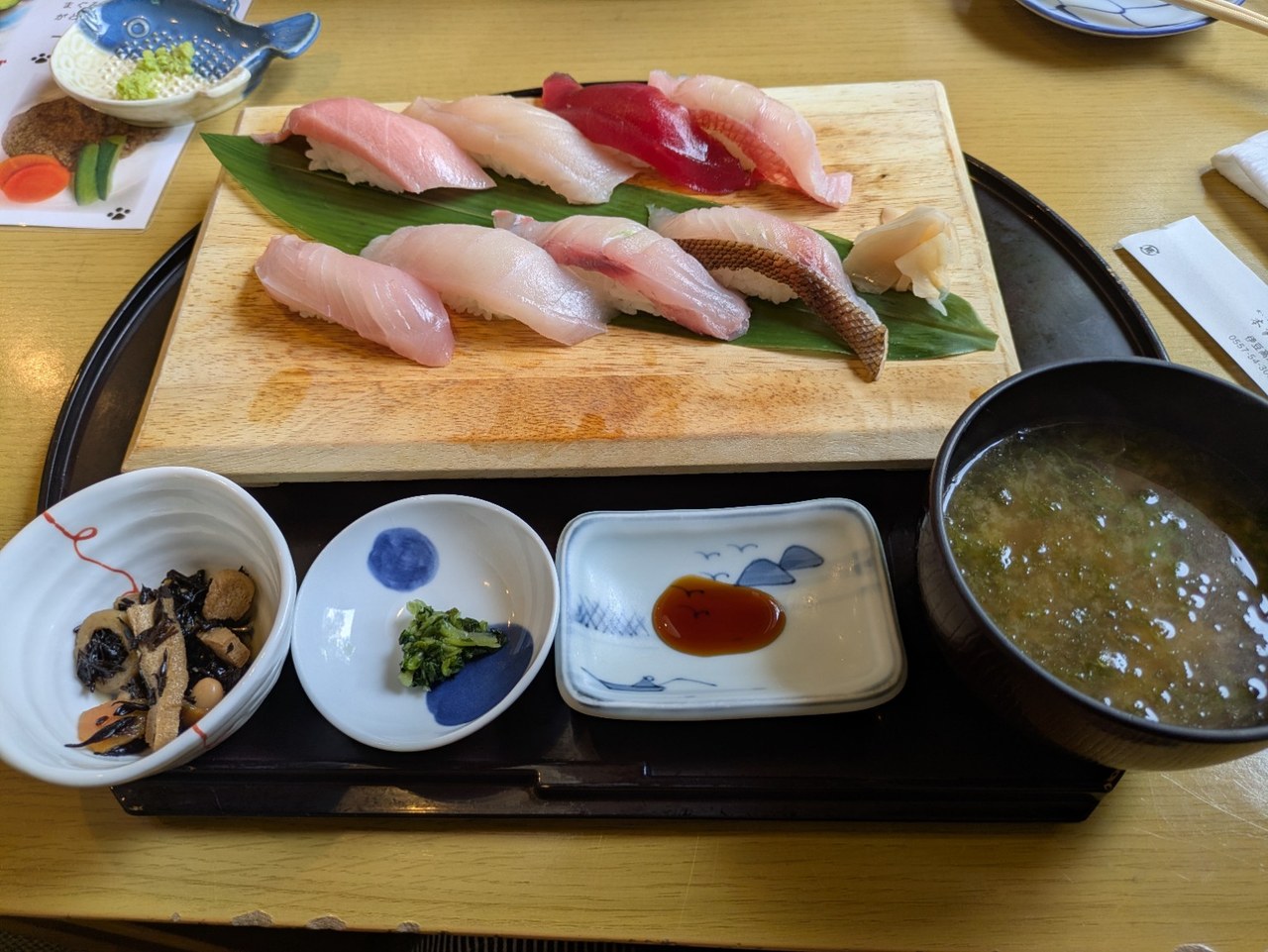 木の板に並んだ握り寿司と、手前の小鉢や味噌汁を載せた御膳